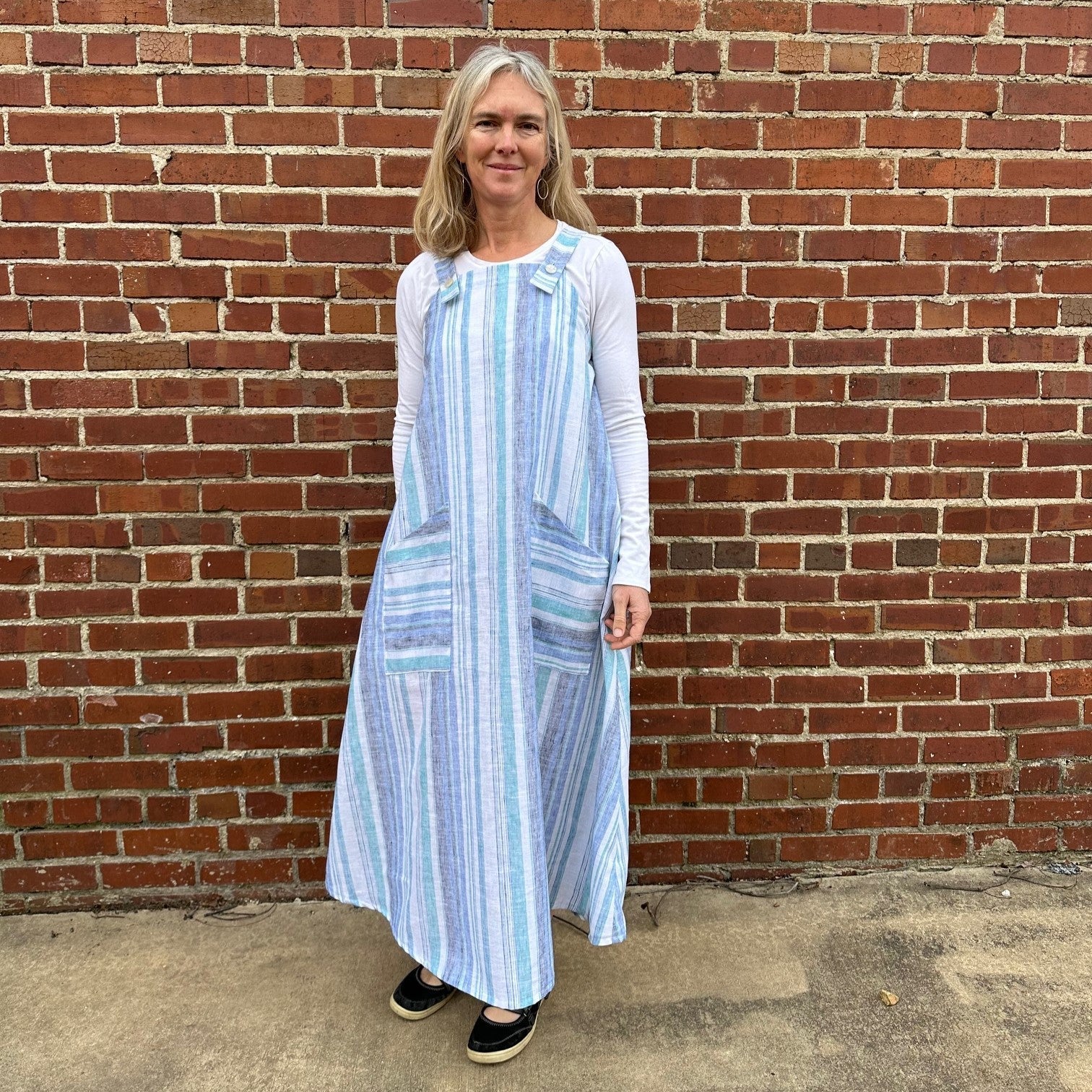 Woman standing in front of a brick wall wearing a blue and white striped dress.