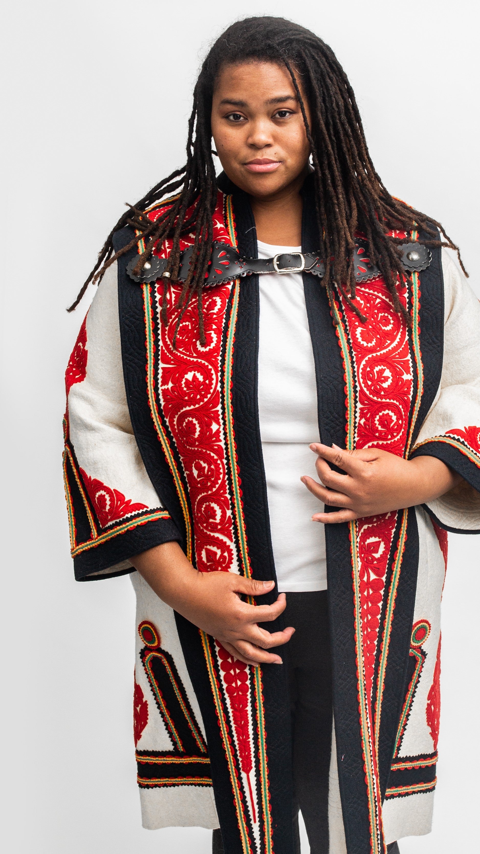 Black woman standing in a traditional szur that is white, black and red wool felt with cutwork applique..