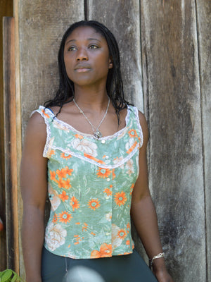 african american woman standing in front of a wood wall wearing a floral green and orange sleeveless camisole.