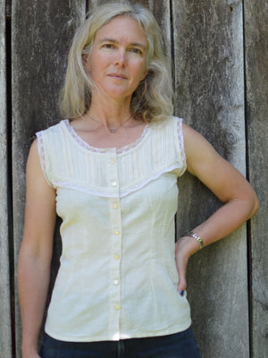 white blonde woman standing in front of a wooden wall with left hand on her hip wearing sleeveless cameo in beige with beige lace embellishment