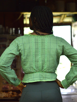 Back of African American woman standing with hands in her hips wearing a green check 234 long sleeved version camisole.
