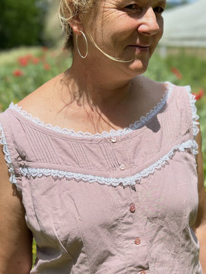 close up of middle aged blonde woman wearing a sleeveless camisole in pale pink with white ruffle lace.