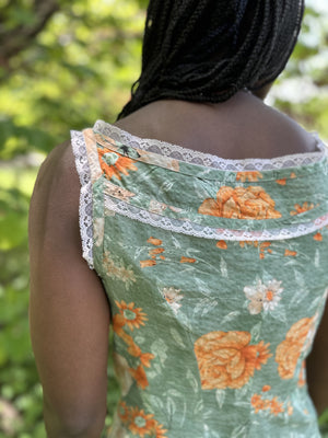 close up of back of sleeveless camisole in floral green and orange, worn by an african american woman with braided hair.