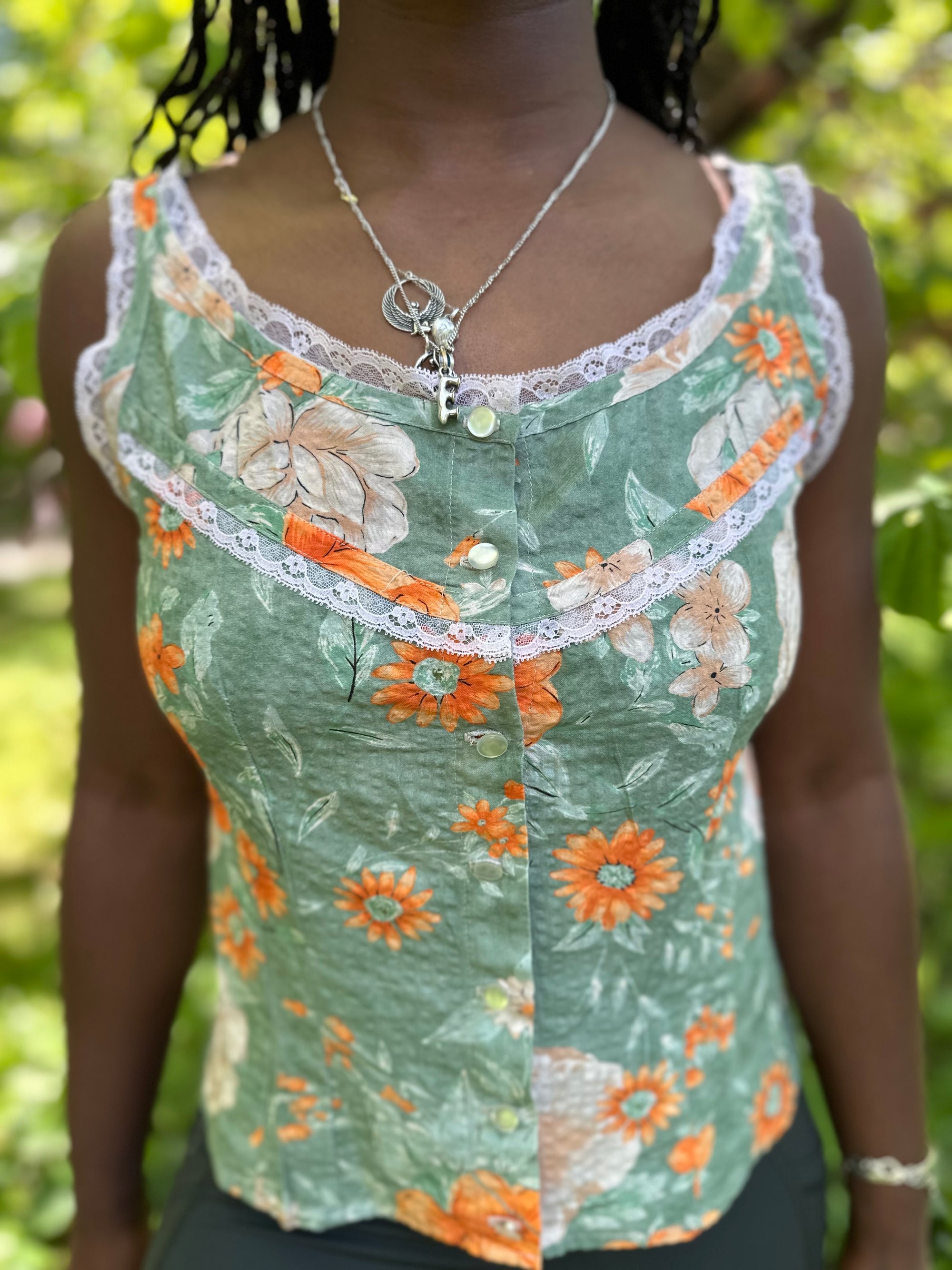 close up of front of sleeveless camisole in floral green and orange, worn by an african american woman with braided hair.