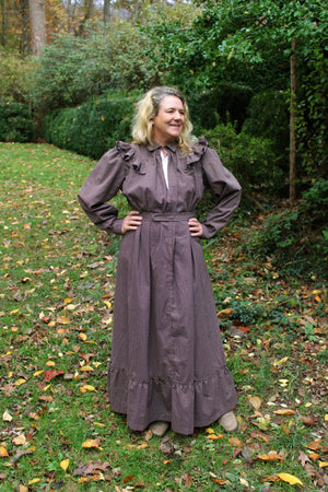 A woman wearing a brown Calico Day Dress standing in lawn outside with her hands on her hips.