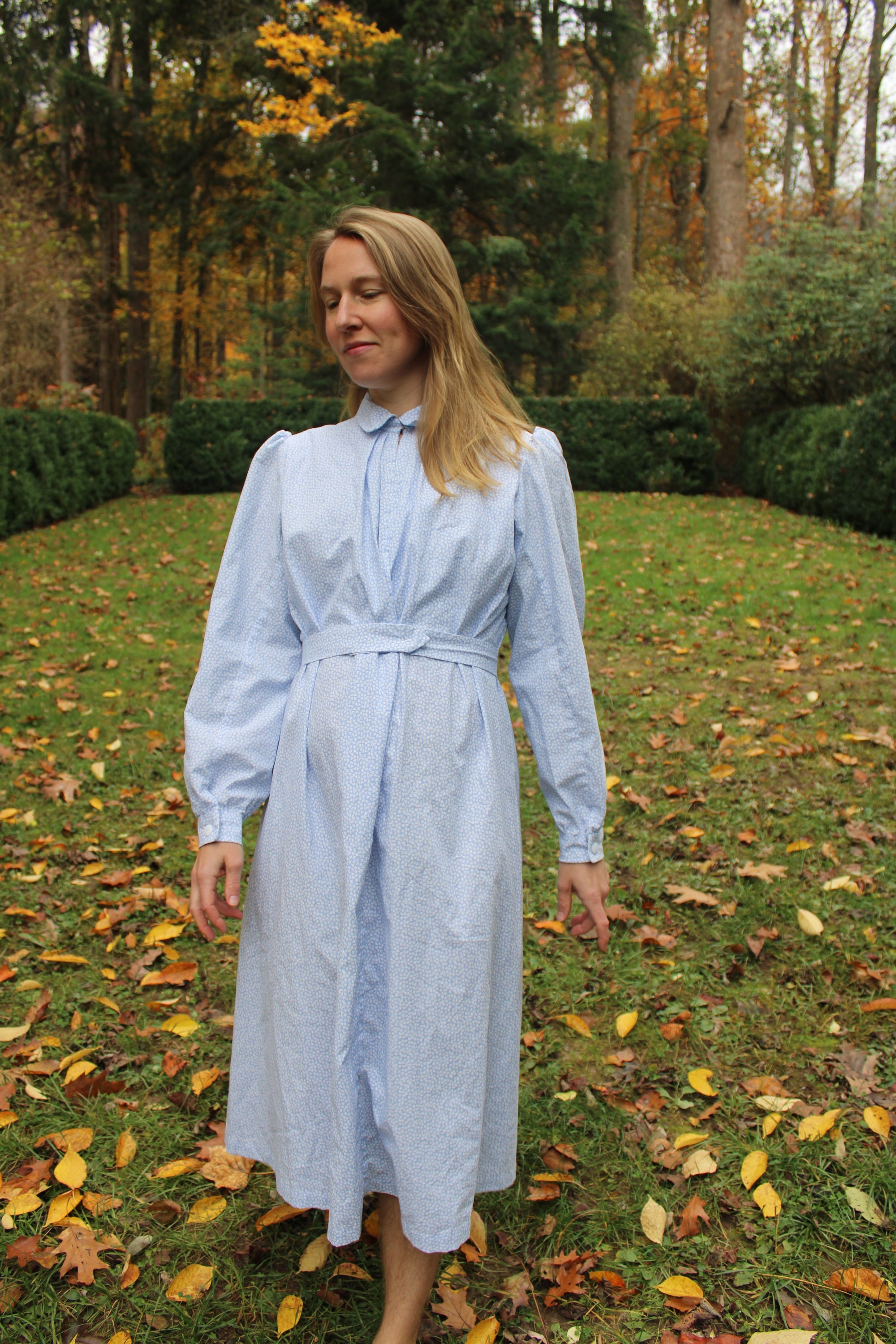 Woman walking in a blue calico Day dress in a lawn.