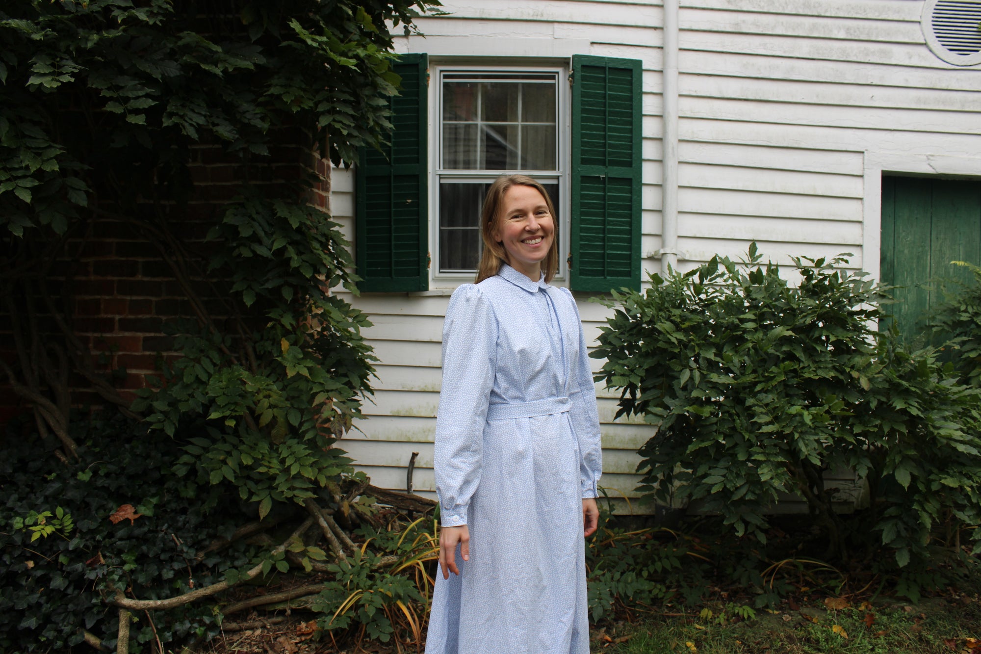 Smiling woman standing in front of a white house in a blue dress