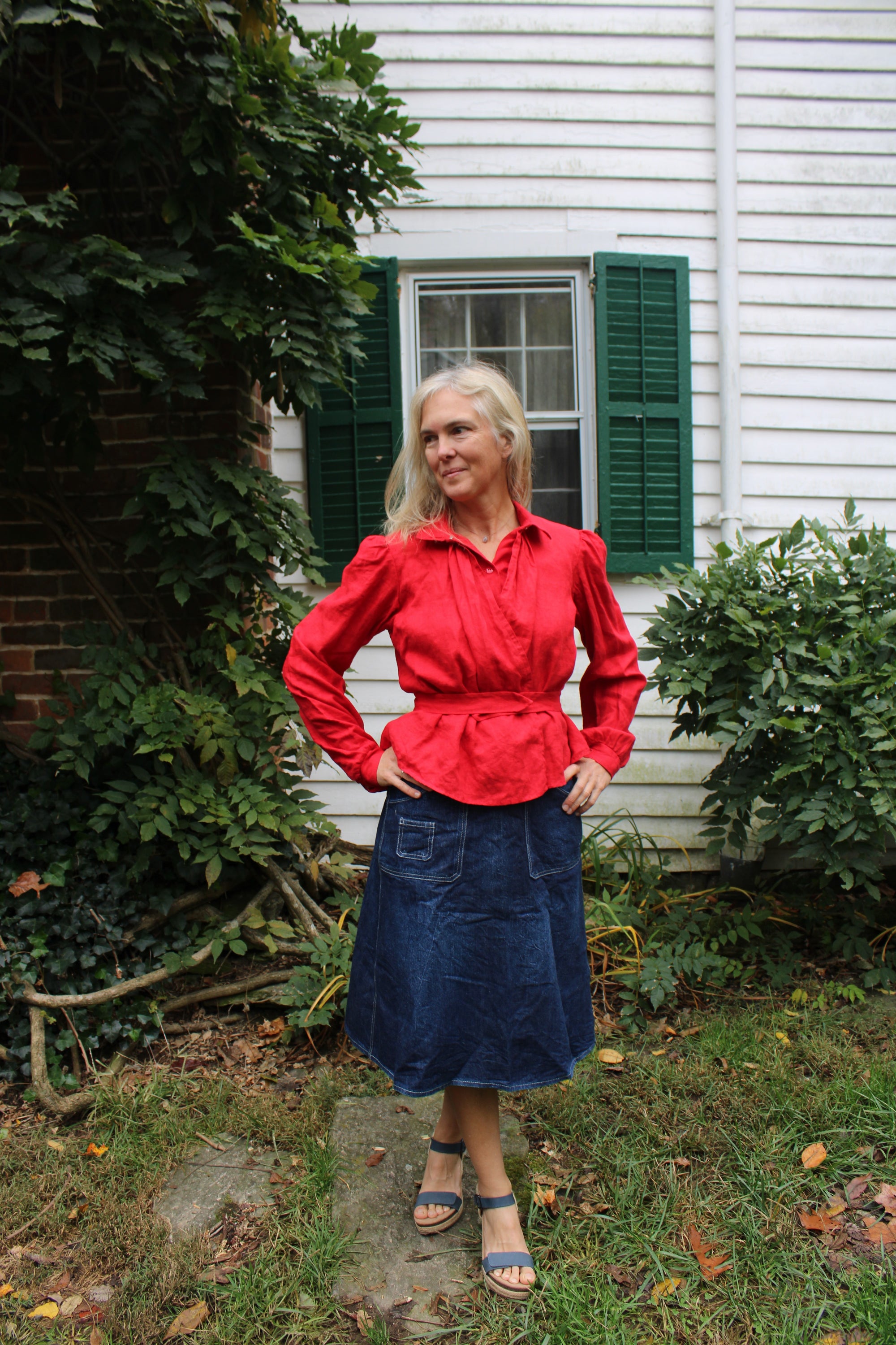 Bright red calico day dress shirt on a woman in a denim skirt in front of a white house.