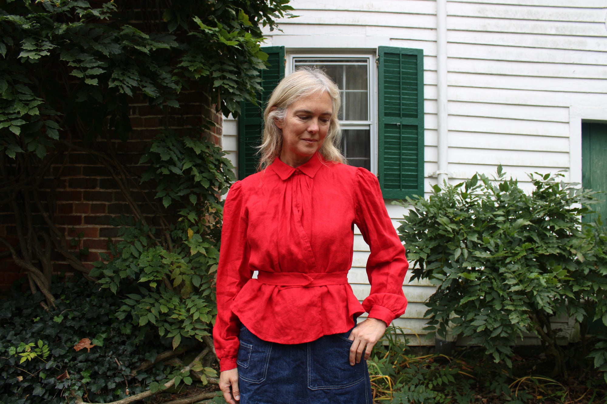 Close up of a woman in a red shirt and denim skirt by white house