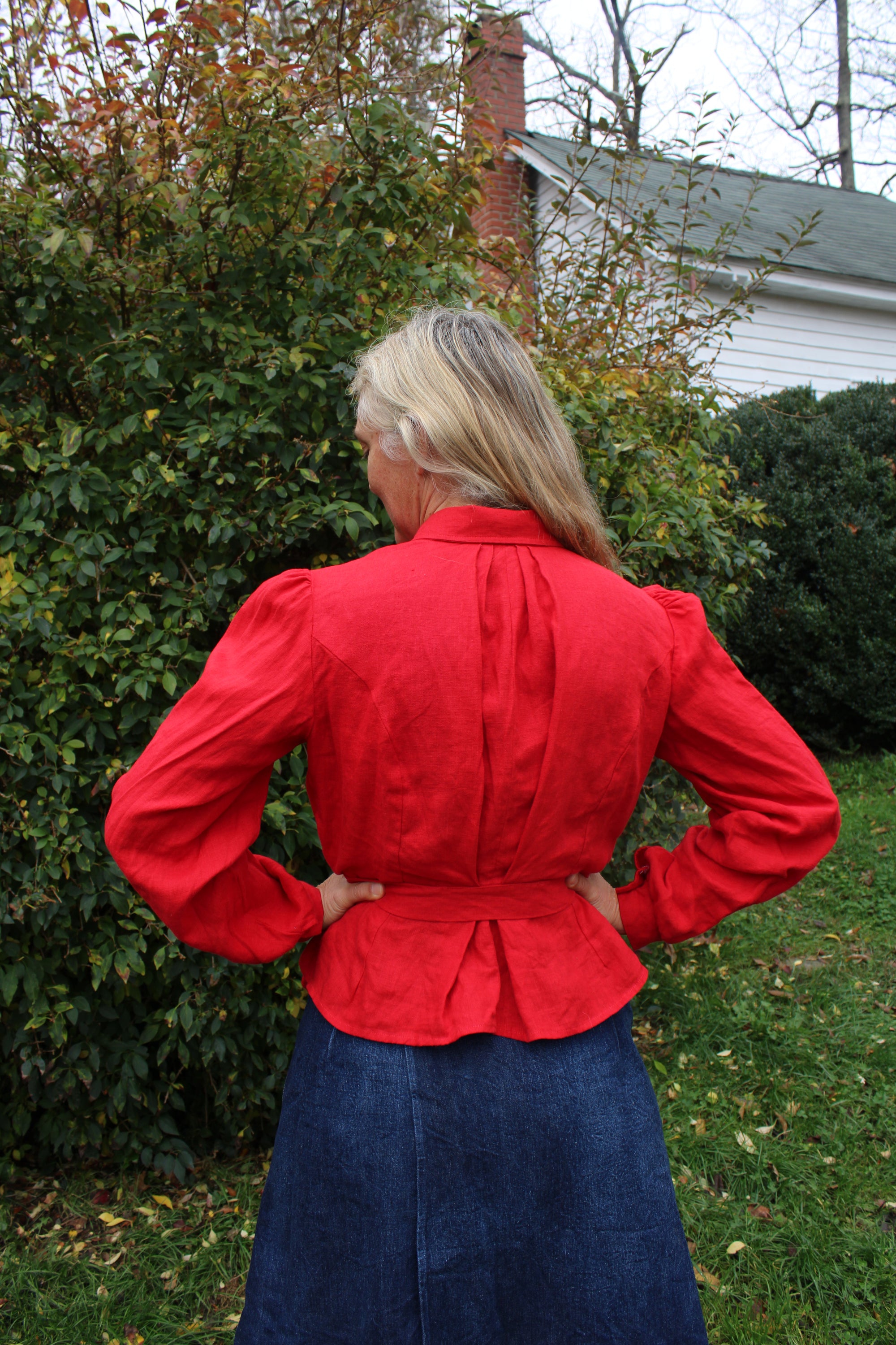 Back of the red shirt on a woman in a lawn. Her hands are on her hips