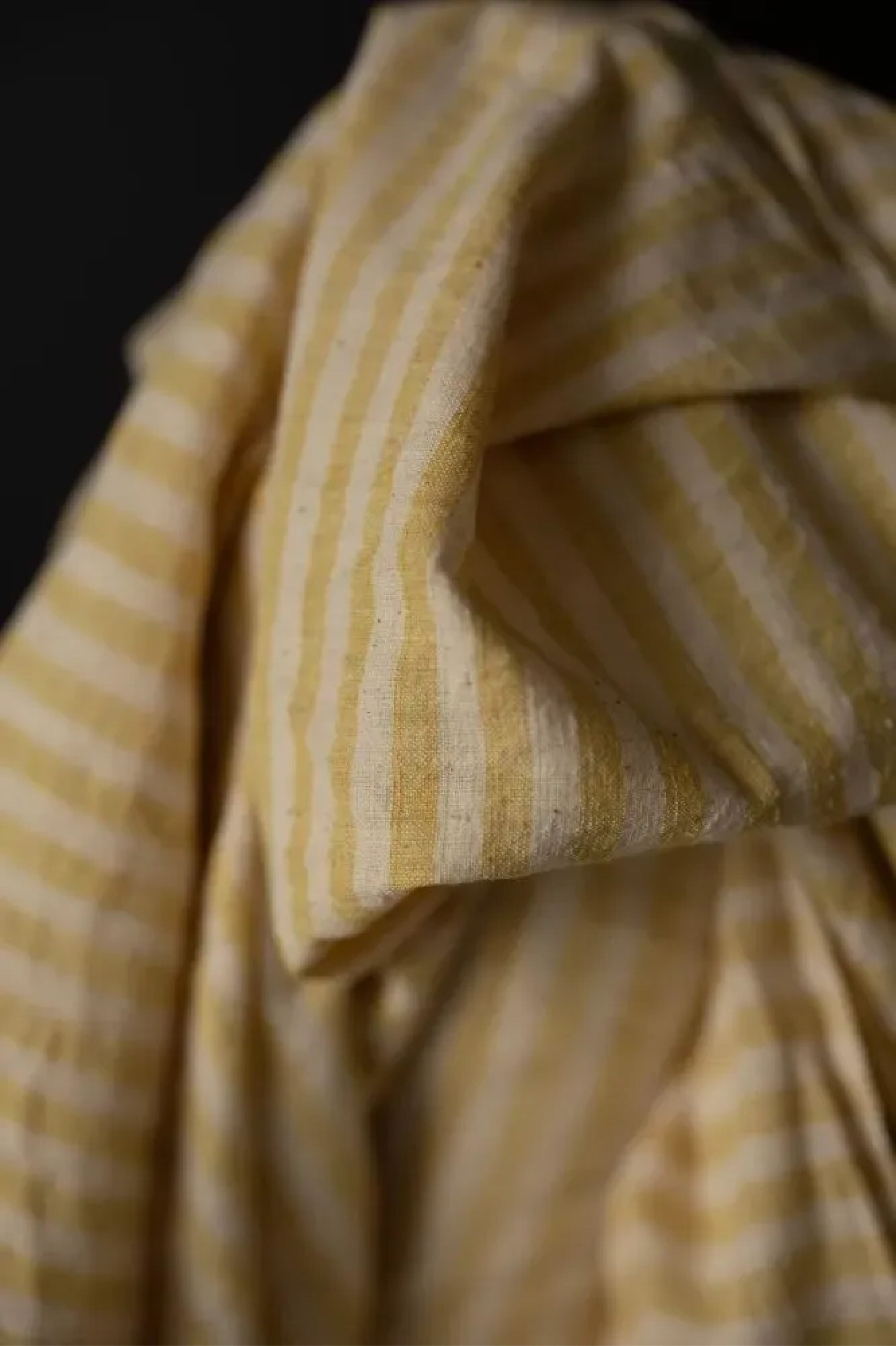 A handloomed sunshine stripe of warm yellow and natural with a loose weave and a washed out slubby texture on a black background.