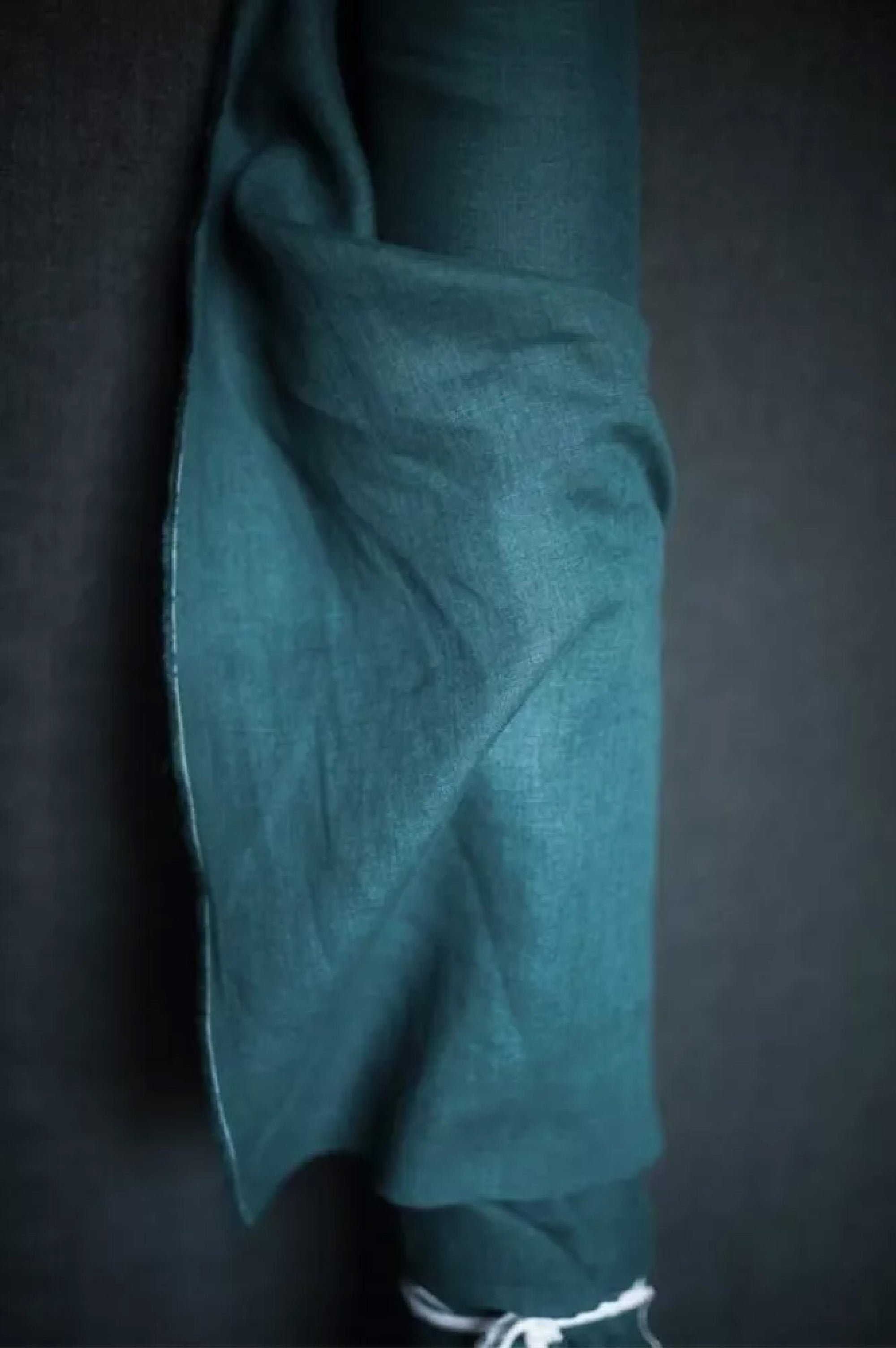 roll of deep blue green linen on a dark grey background.