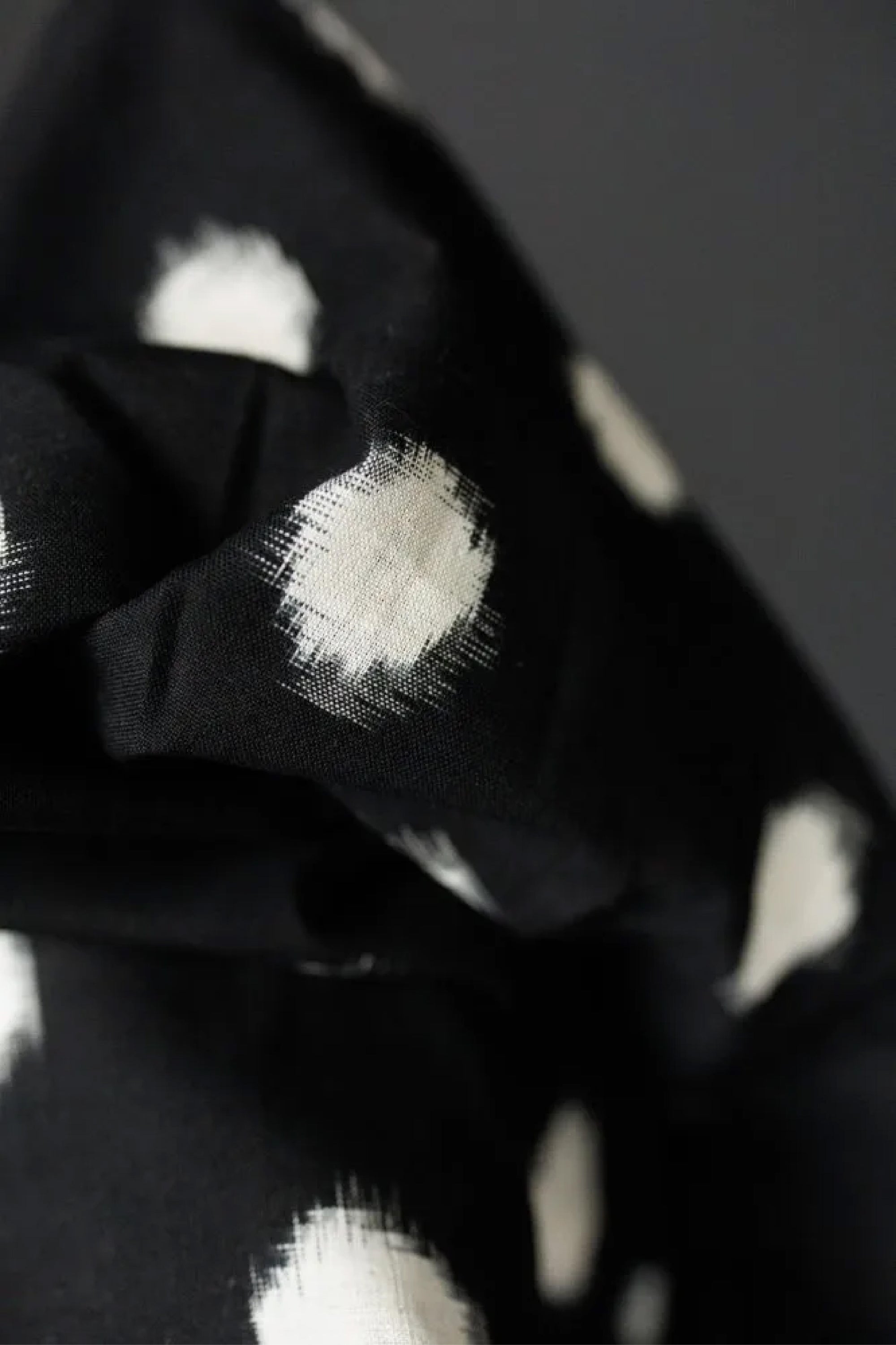 close up of Bold monocrome Ikat with a black background and off white spot fabric on a dark grey background.