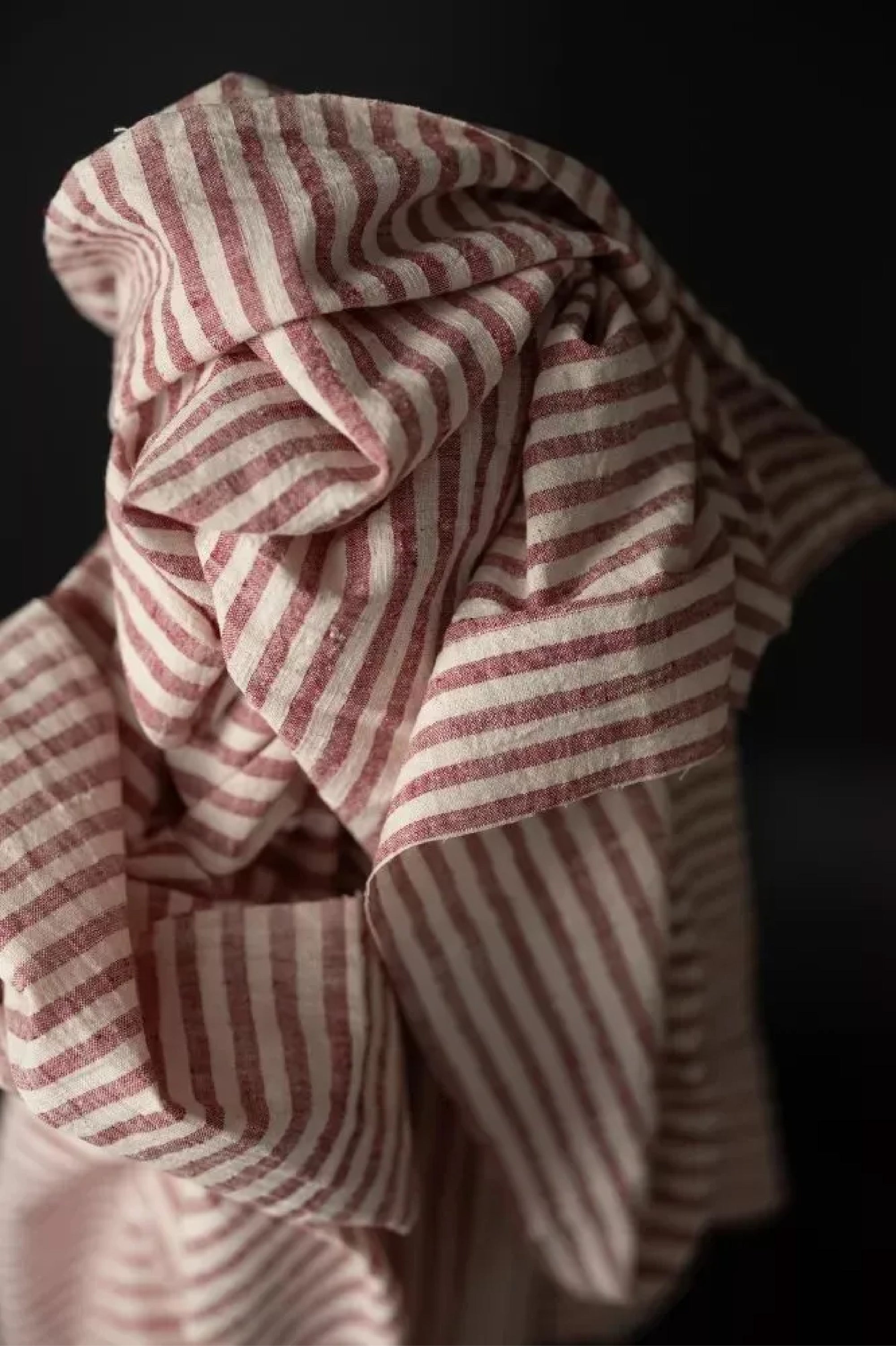 close up A handloomed candy stripe of dusty red and natural with a loose weave and a washed out slubby texture fabric on a dark grey background.