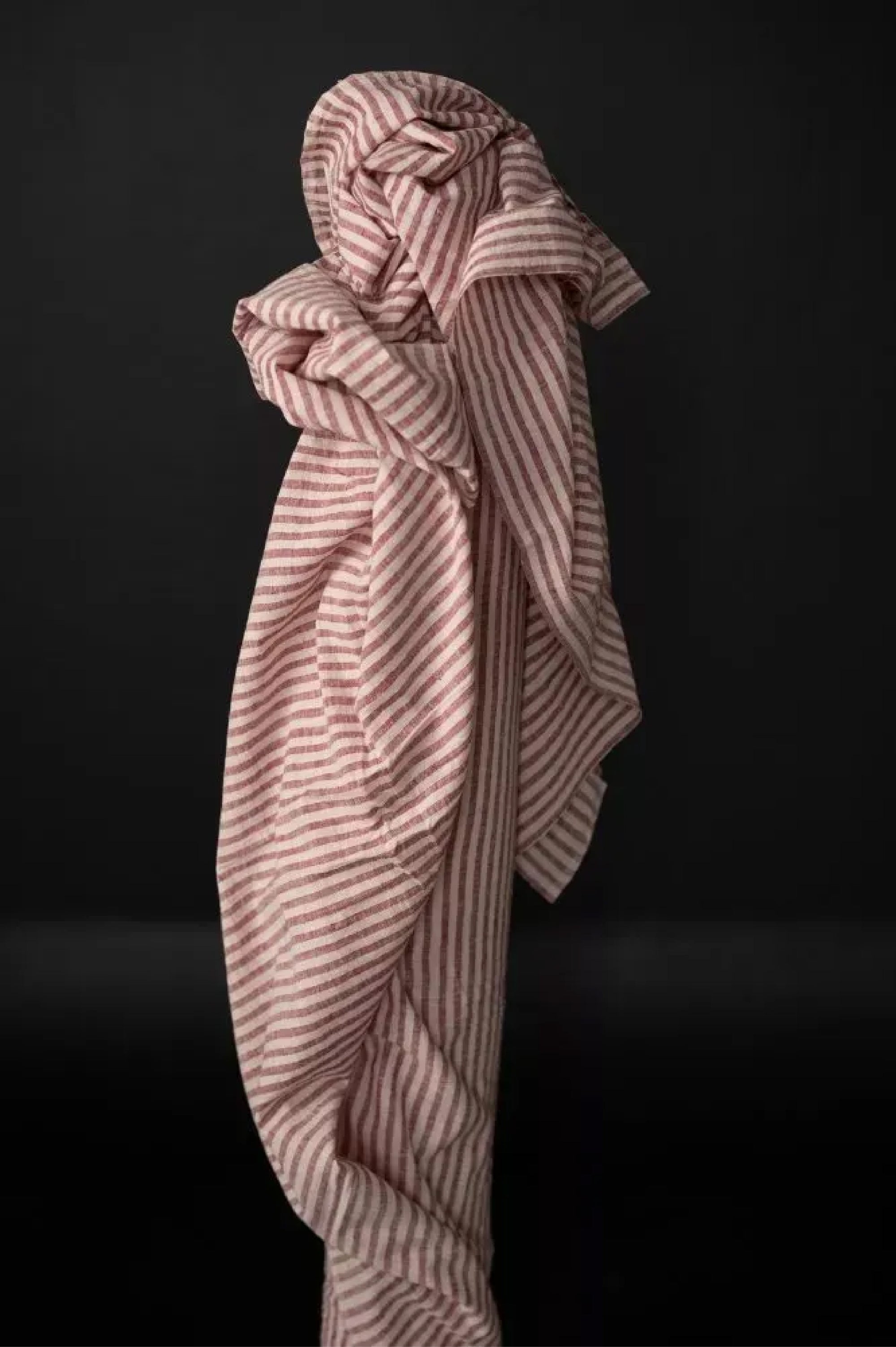 A handloomed candy stripe of dusty red and natural with a loose weave and a washed out slubby texture fabric on a dark grey background.