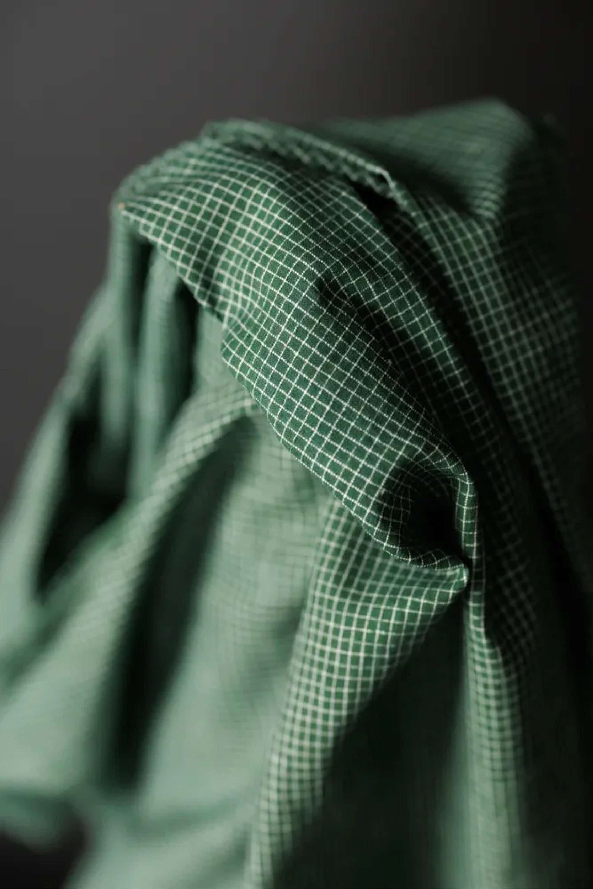 A dark forest green mini check indian cotton fabric on a dark grey background.